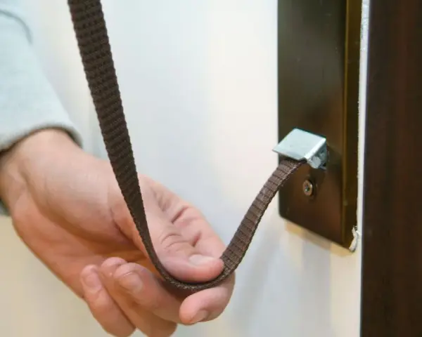 Mano sujetando una cinta marrón que se ha roto la cuerda de la persiana, enganchada a un soporte metálico.