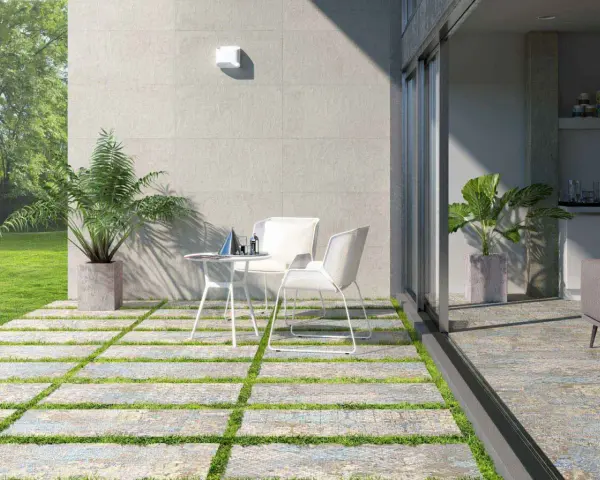 Terrazas pequeñas con encanto: un camino de baldosas y césped lleva a una mesa y sillas blancas, con plantas y un jardín verde.