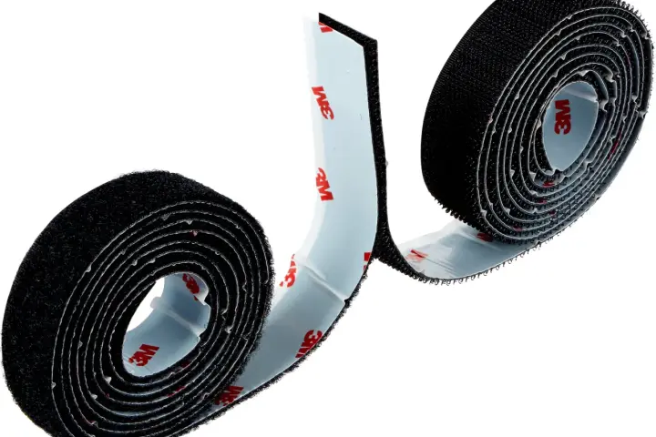 Dos rollos de cinta adhesiva negra, que es velcro, con el logo de 3M en el reverso.
