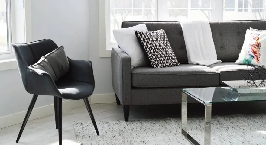 Un sillón negro y un sofá gris con cojines decorativos, listos para aprender como tapizar un sofa y renovar tu sala.