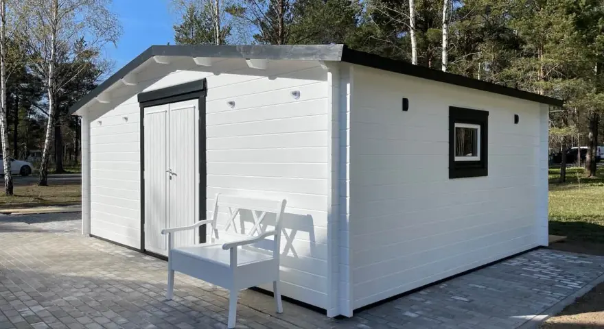 Caseta blanca con puerta doble y ventana, ideal para hacer caseta con palets. Un banco blanco invita a sentarse.