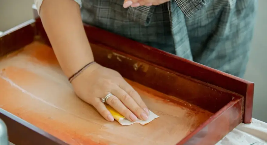Mano limpiando un cajón de madera antiguo con un paño. Un paso esencial para saber como limpiar muebles de madera antiguos.
