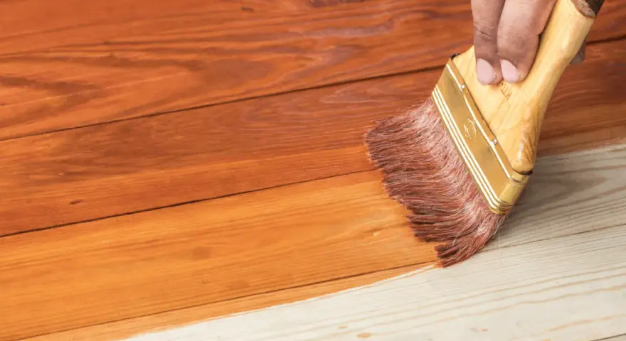 Aplicando barniz a una casa de madera para su mantenimiento. La brocha extiende el producto sobre las tablas.