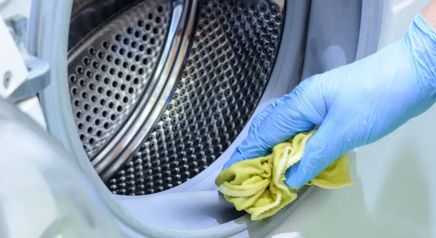 Mano con guante azul limpiando la goma de la lavadora con un paño amarillo. Un método natural para limpiar lavadora vinagre y bicarbonato.