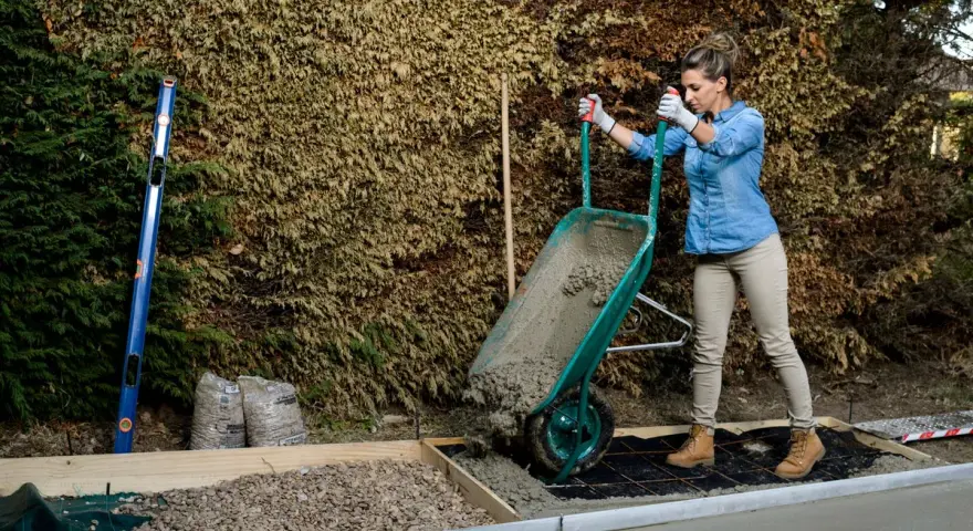 Mujer vertiendo hormigón de carretilla para como hacer una base de hormigon. Se ven herramientas y materiales de construcción.