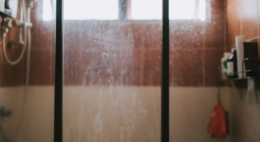 Vidrio de ducha sucio, con marcas de agua y jabón. Un recordatorio visual de cómo limpiar cristales para un baño reluciente.