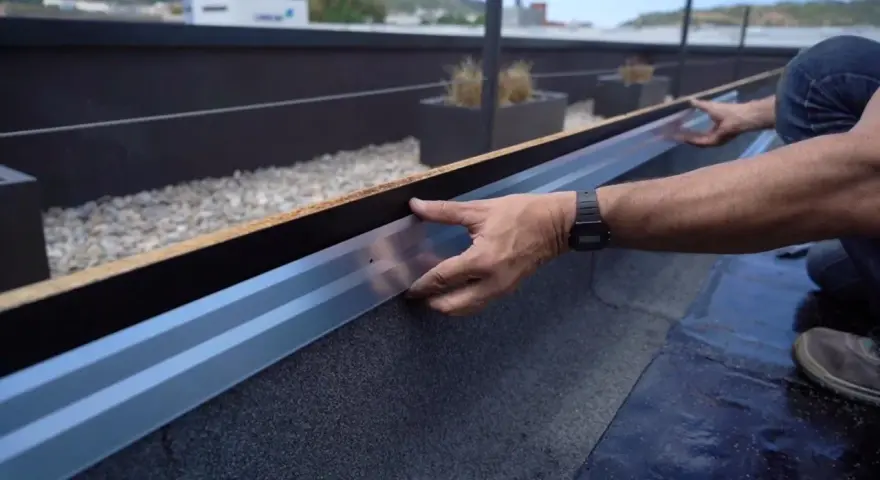 Instalación de tela asfáltica en tejado, un operario ajusta un perfil metálico.