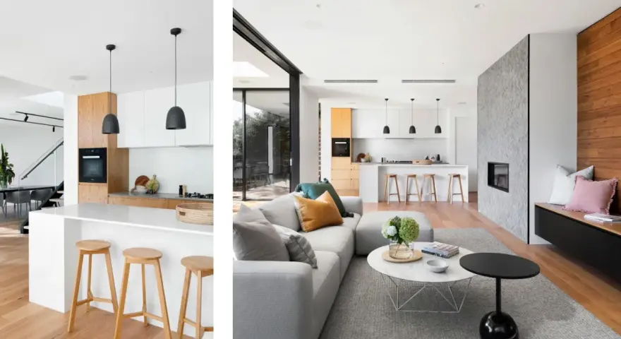 Cocina tipo americana moderna con isla, taburetes de madera y sala de estar contigua con chimenea de piedra.