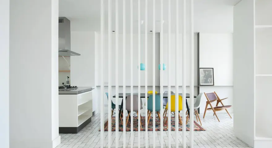 Elegante solución para dividir salón en dos ambientes con un separador de lamas blancas. Cocina moderna y comedor con sillas de colores.