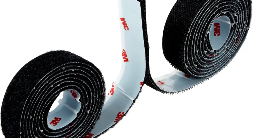 Dos rollos de cinta adhesiva negra, que es velcro, con el logo de 3M en el reverso.