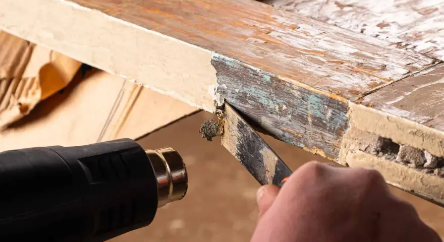 Se usa una pistola de calor para ablandar pintura vieja y descascarada de un marco de madera, facilitando su retirada con una espátula. La madera se hincha con el calor.