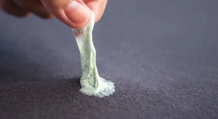 Mano retirando chicle pegado a tela. Aprende como quitar chicle de la ropa fácilmente.