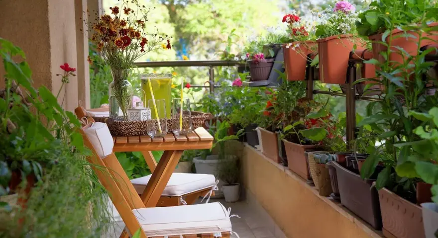 Un balcón acogedor con mesa de madera, sillas, jarra de limonada y muchas plantas. La decoración de mini balcones crea un oasis verde.