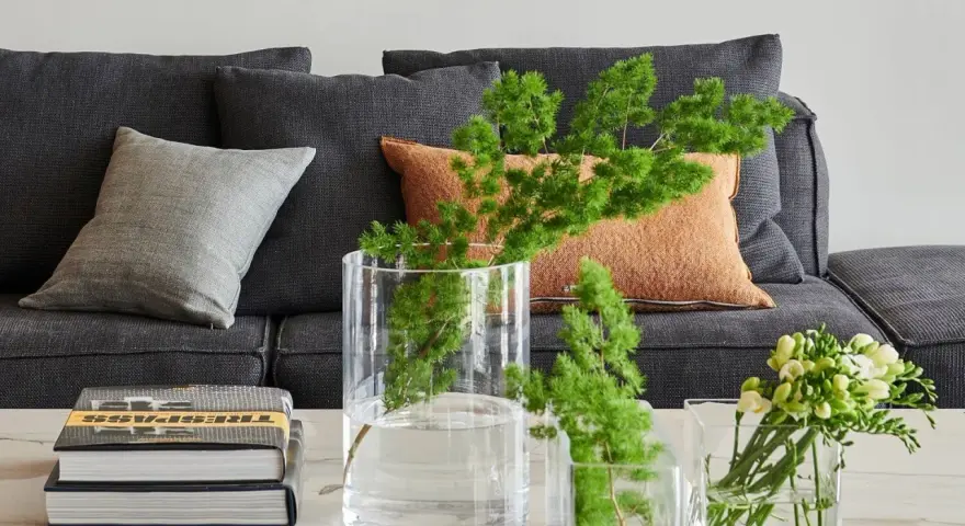 Ideas para decorar mesa de centro rectangular: jarrones con ramas verdes y flores, junto a libros apilados.