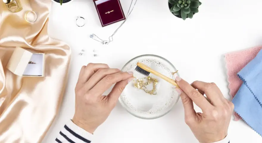 Manos limpian una cadena de oro con un cepillo en agua jabonosa. Aprende como limpiar el oro para que brille como nuevo.