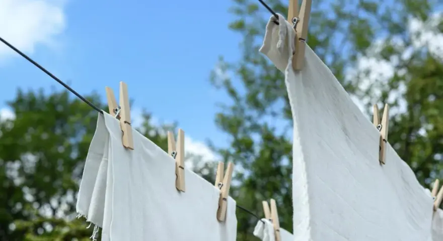 Ropa blanca desteñida de azul secándose al sol, sujeta con pinzas de madera a un tendedero.
