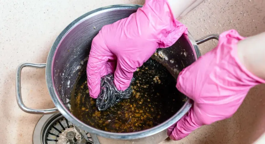 Manos con guantes rosas frotando una olla quemada con estropajo. Un reto para saber como quitar el quemado de una olla.