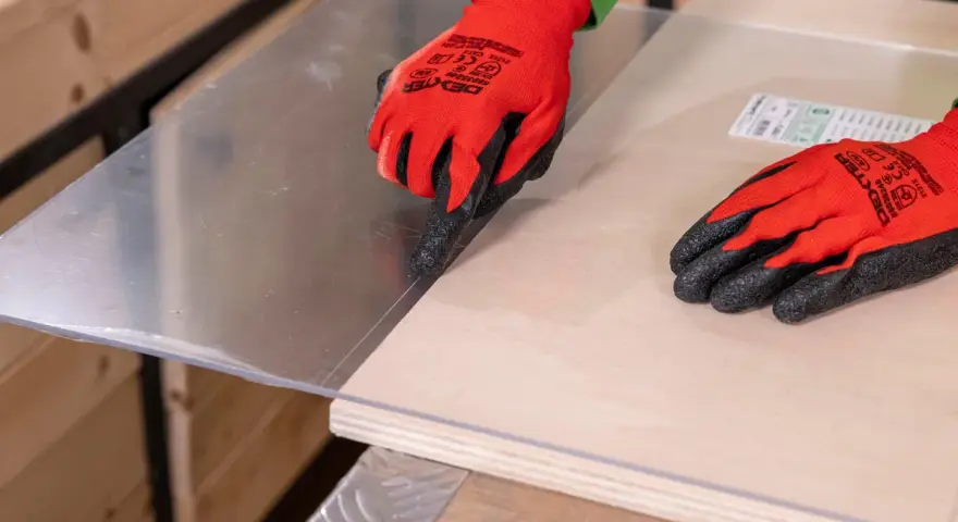 Manos con guantes rojos marcan el metacrilato sobre madera, mostrando cómo se corta el metacrilato con precisión.