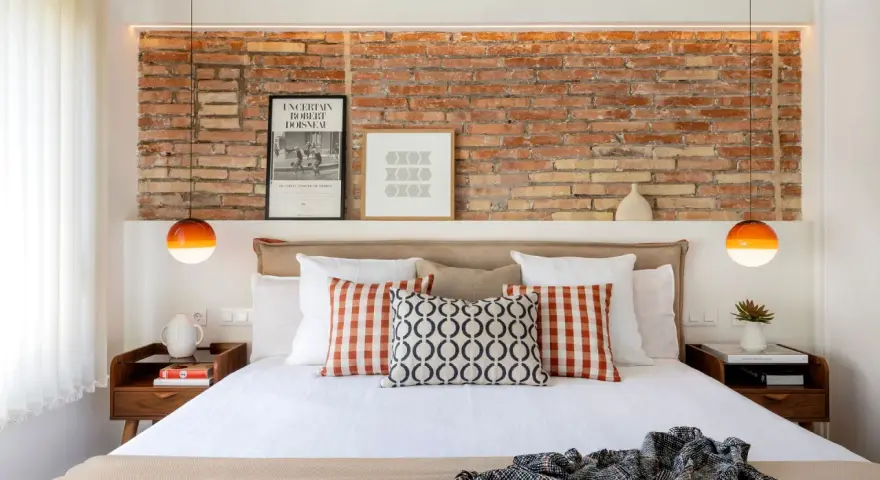 Ideas para decorar pared cabecero cama: ladrillo visto, cuadros modernos y lámparas naranjas.