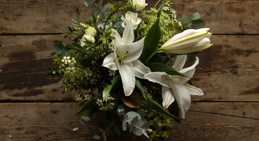 Un ramo de lirios blancos y rosas sobre madera rústica. La pregunta de cuanto dura un ramo de flores depende de su cuidado.