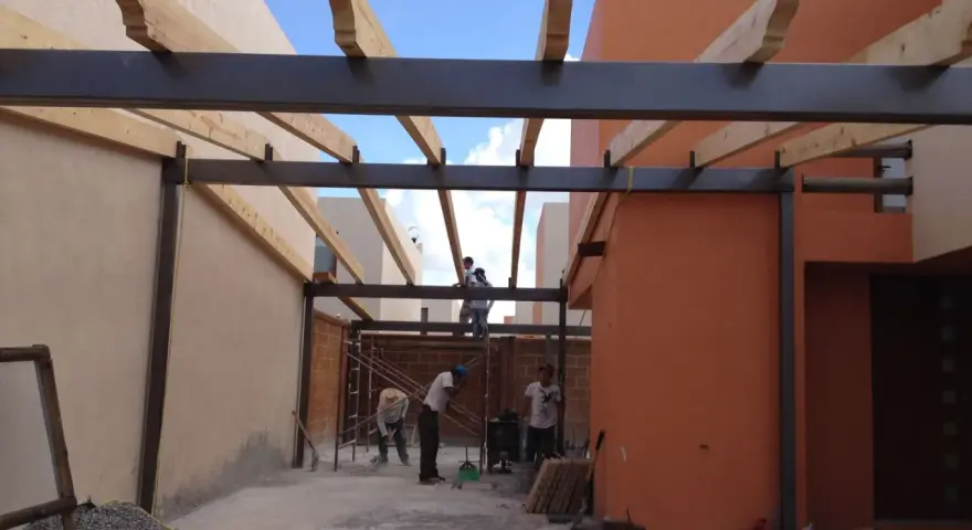 Trabajadores construyen la estructura de un garaje, instalando vigas de metal y madera.