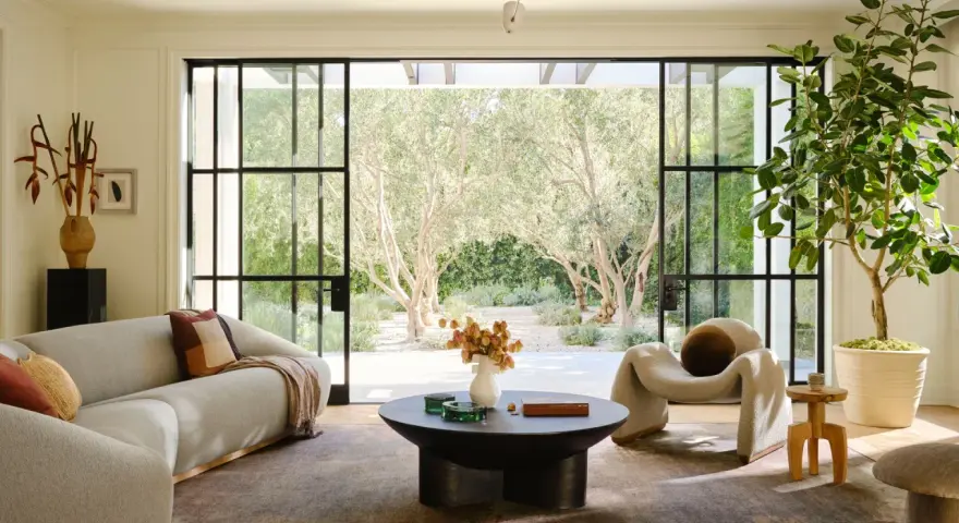 Salones modernos y elegantes con sofá curvo, sillón acogedor y mesa de centro, con vistas a un jardín de olivos.