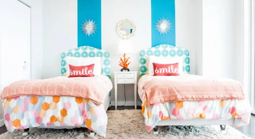 Dos camas gemelas en habitaciones pequeñas, decoradas con cojines que dicen "smile" y ropa de cama colorida.