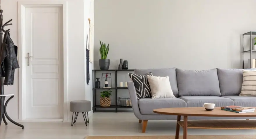 Un salón moderno con sofá gris, mesa de centro de madera y puerta blanca. El suelo claro ayuda a combinar suelo y puertas, creando un espacio luminoso.