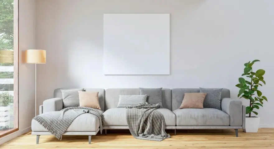 Sofá gris con cojines en tonos tierra y grises, mantas y planta verde. Ideas para combinar cojines con sofá gris.