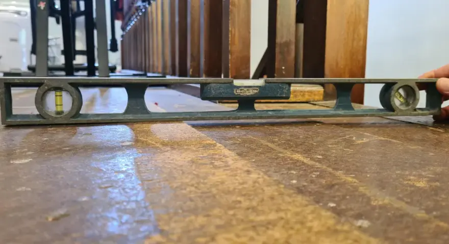 Nivelando un suelo de madera antiguo con un nivel de burbuja. La herramienta muestra que el suelo está ligeramente inclinado.