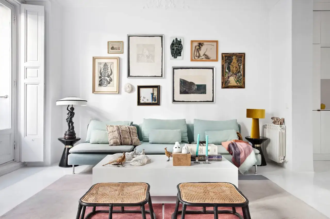 Un sofá azul pálido con cojines y mantas, decorado con cuadros y figuras. Ideas de que poner detras del sofa para un estilo ecléctico.