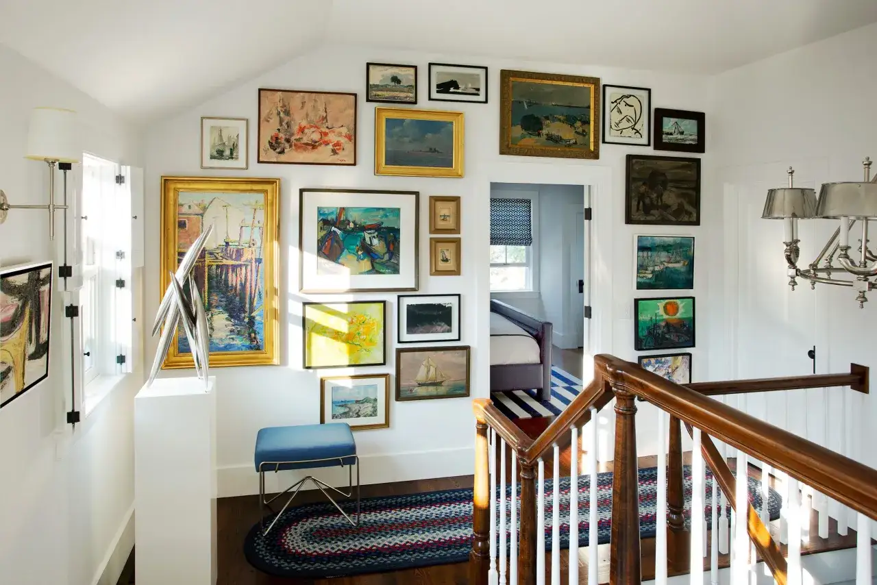 Ideas para colocar cuadros en un pasillo largo y estrecho: una pared llena de arte marino y paisajes, creando un corredor de galería.