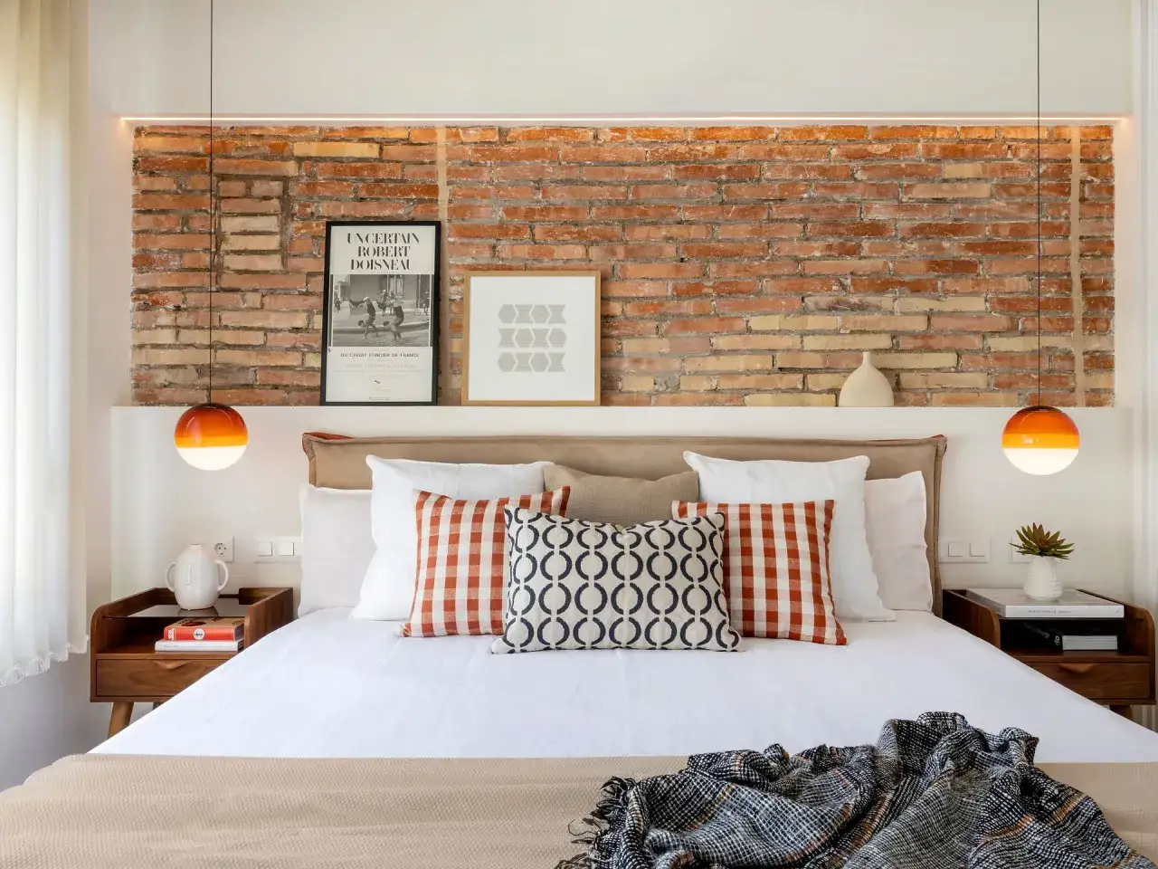 Ideas para decorar pared cabecero cama: ladrillo visto, cuadros y lámparas naranjas.