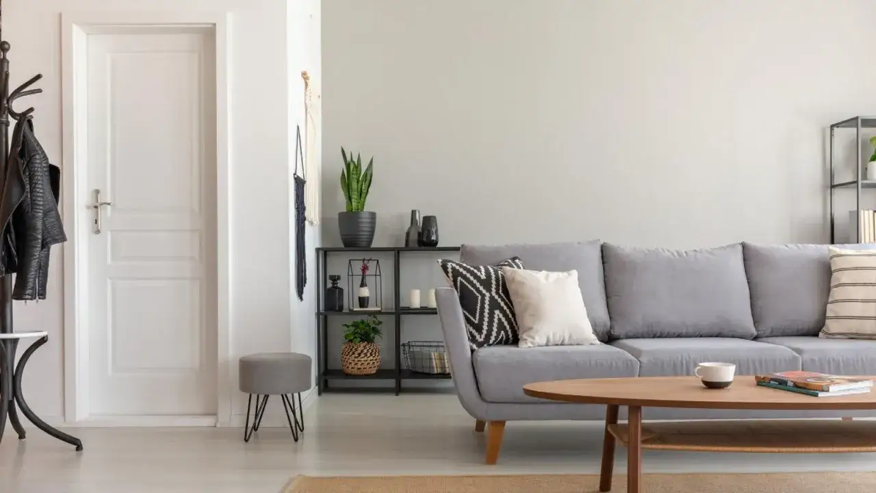 Un sal&oacute;n moderno con sof&aacute; gris, mesa de centro de madera y puerta blanca. El suelo claro ayuda a combinar suelo y puertas, creando un espacio luminoso.