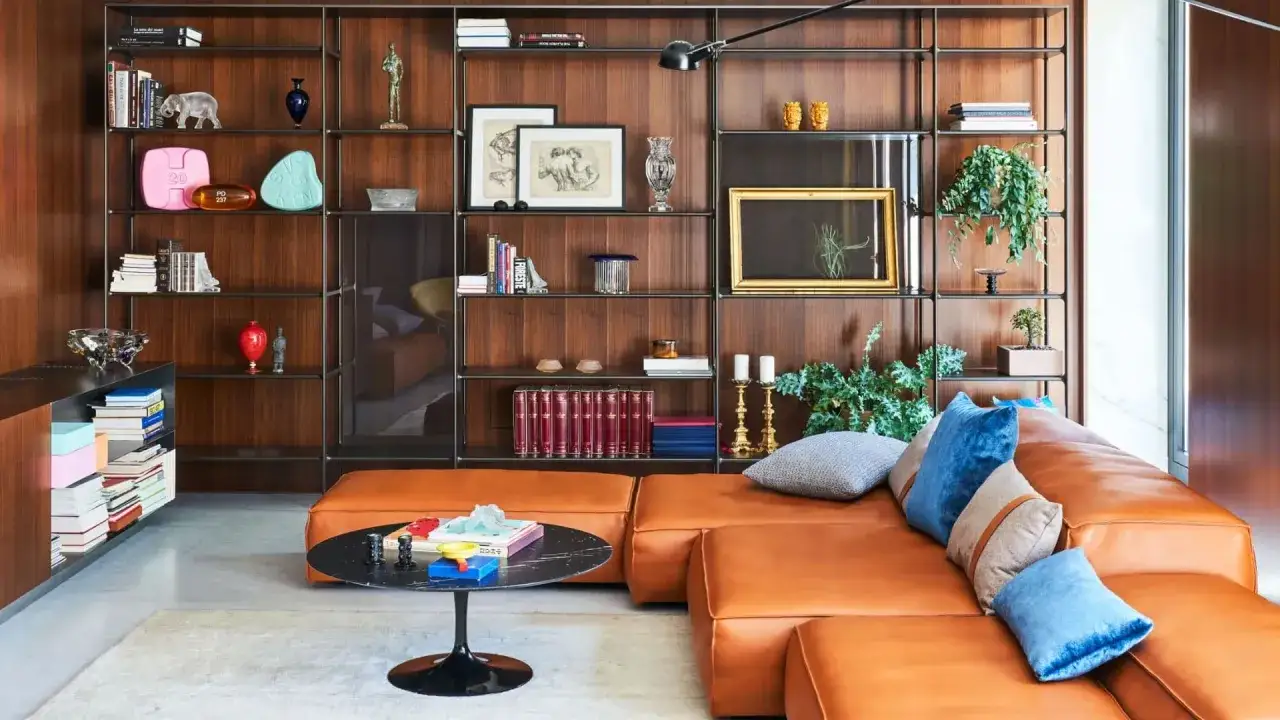Sofá naranja y estantería de madera con objetos decorativos, todo con un marcado estilo mid century.