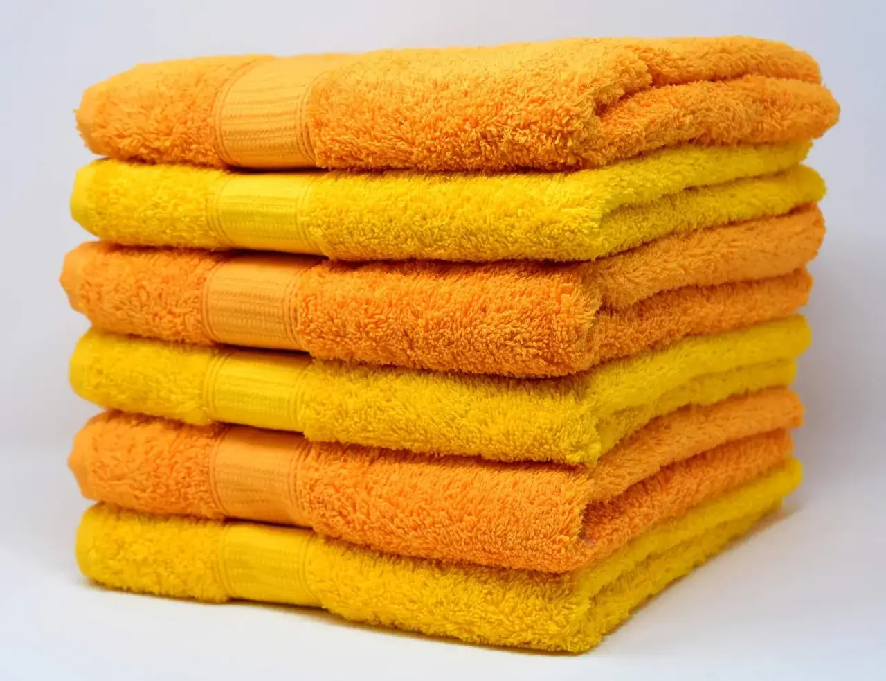 Pila de toallas naranjas y amarillas, esponjosas y suaves. Descubre c&oacute;mo lavar toallas para que queden suaves y perfectas.