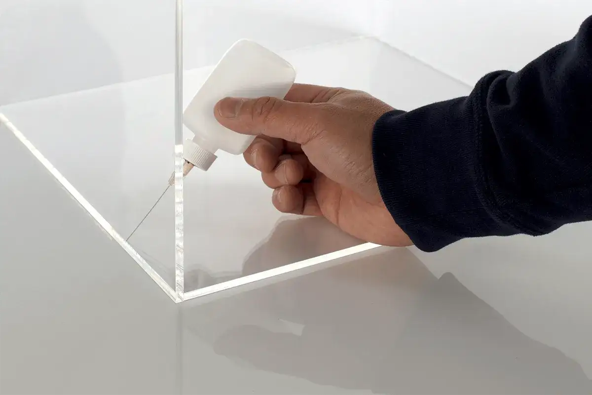 Mano aplicando adhesivo con precisión para saber como pegar el metacrilato y crear uniones perfectas.