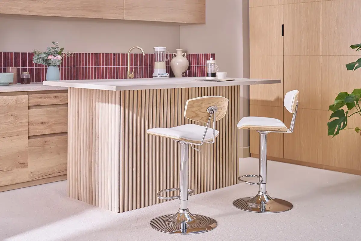 Dos taburetes de barra con asiento blanco y respaldo de madera, con una altura de taburete de barra de 90 cm, junto a una isla de cocina con base de listones de madera.