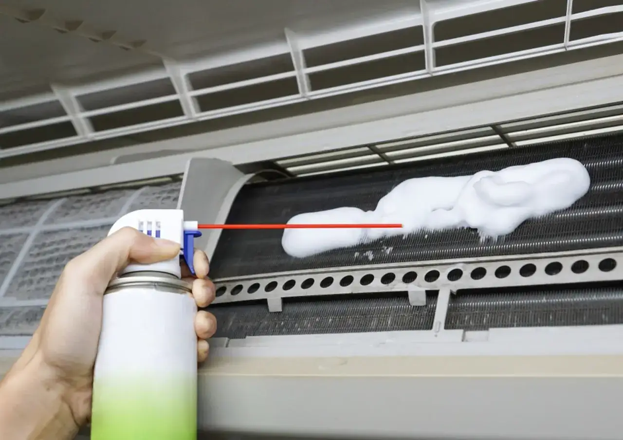 Mano rociando espuma para limpiar aire acondicionado por dentro.