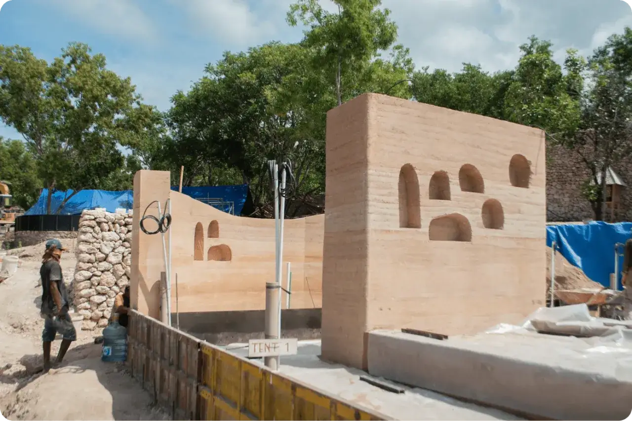 Construcci&oacute;n de muros de tierra apisonada con nichos. Se observa un trabajador y materiales para hacer suelo de cemento sobre tierra.
