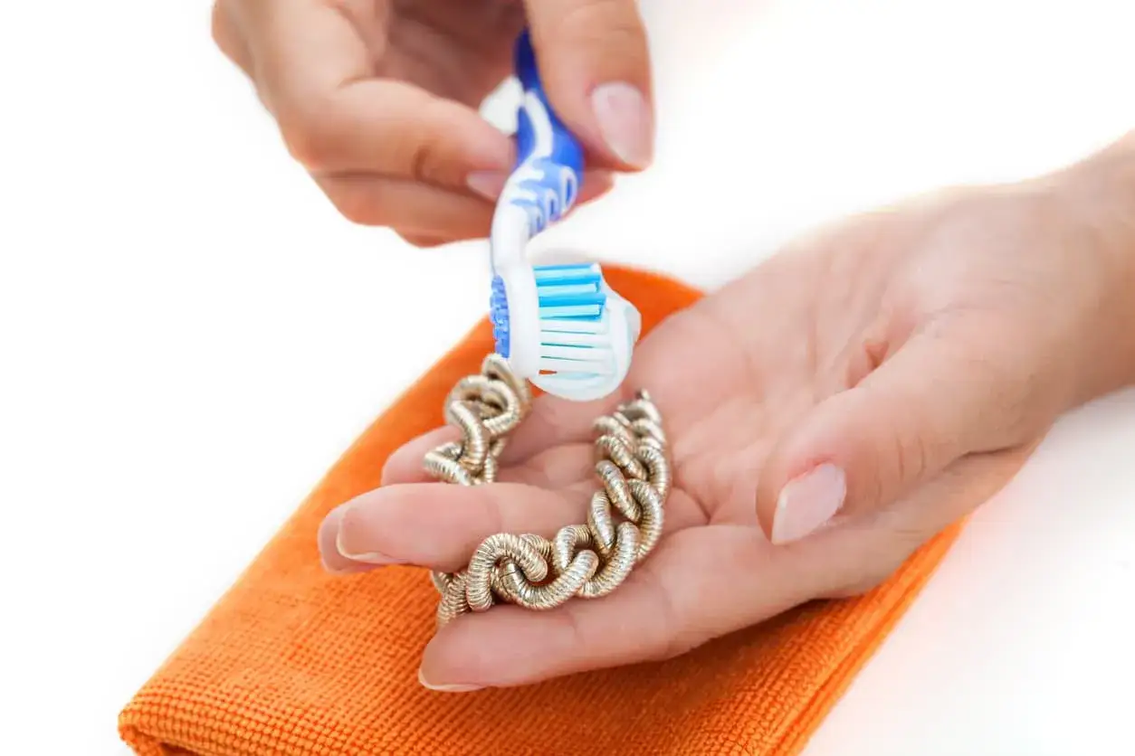 Manos limpiando una pulsera de oro con un cepillo de dientes. Aprende como limpiar el oro para que brille como nuevo.