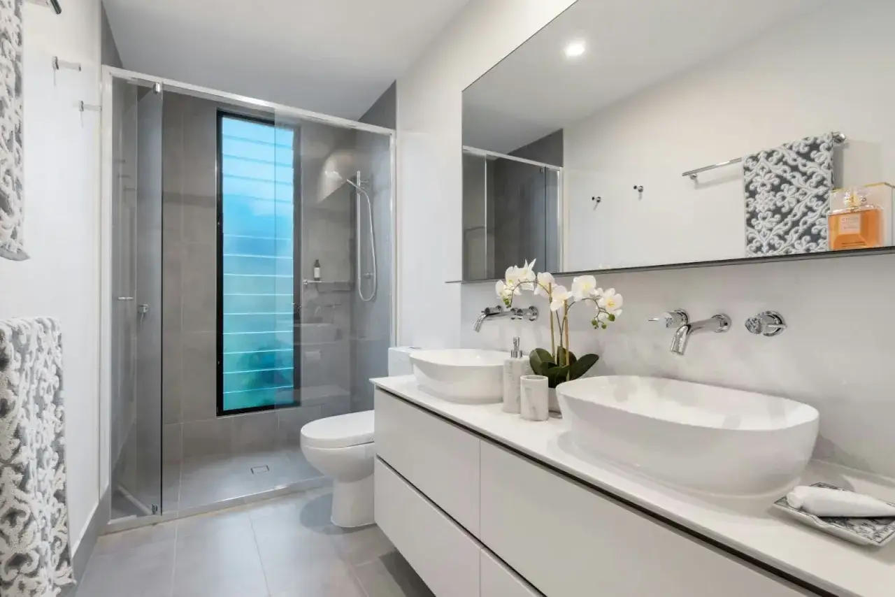 Ideas para como decorar un ba&ntilde;o moderno: ducha con mampara, inodoro, lavabo doble sobre mueble blanco, espejo grande y orqu&iacute;deas.