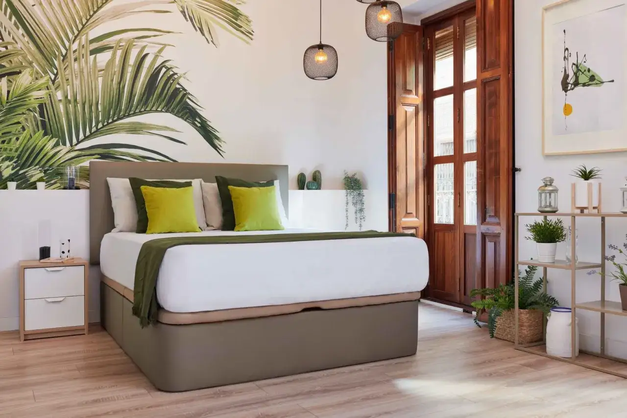 Cama con cabecero tapizado y dosel de almacenamiento, ideal para un dormitorio con estilo feng shui. Pared con mural de hojas tropicales.
