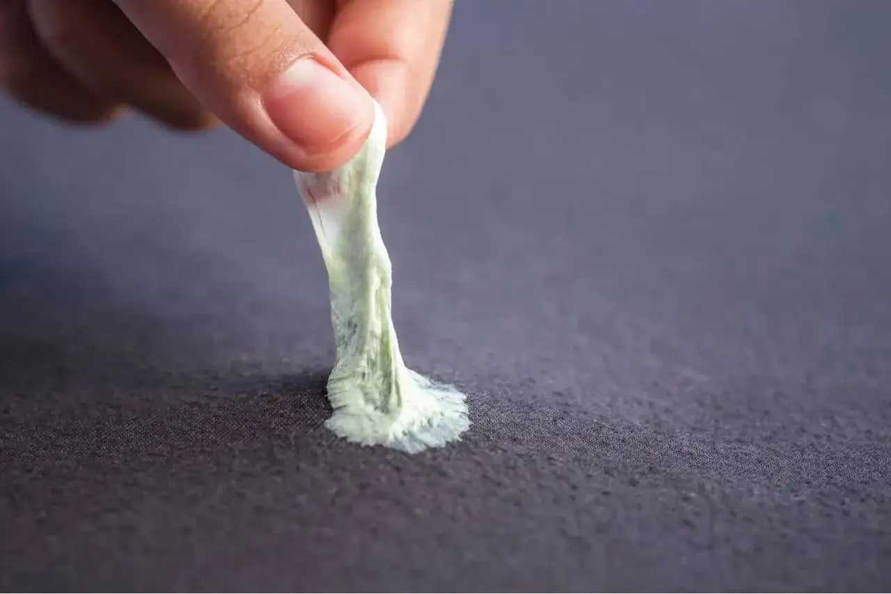 Mano retirando chicle pegado a tela. Aprende como quitar chicle de la ropa fácilmente.