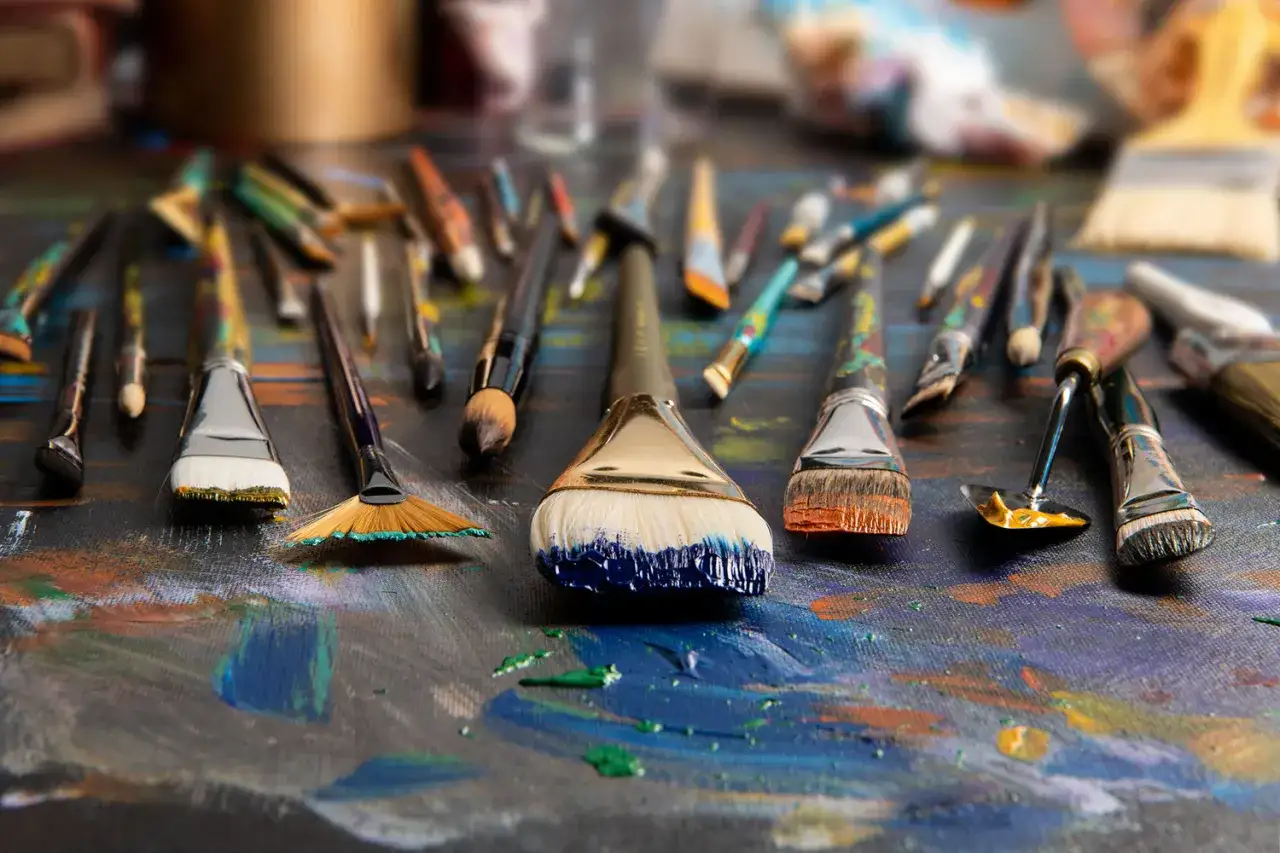 Variedad de tipos de pinceles, algunos con restos de pintura azul y naranja, listos para crear arte.
