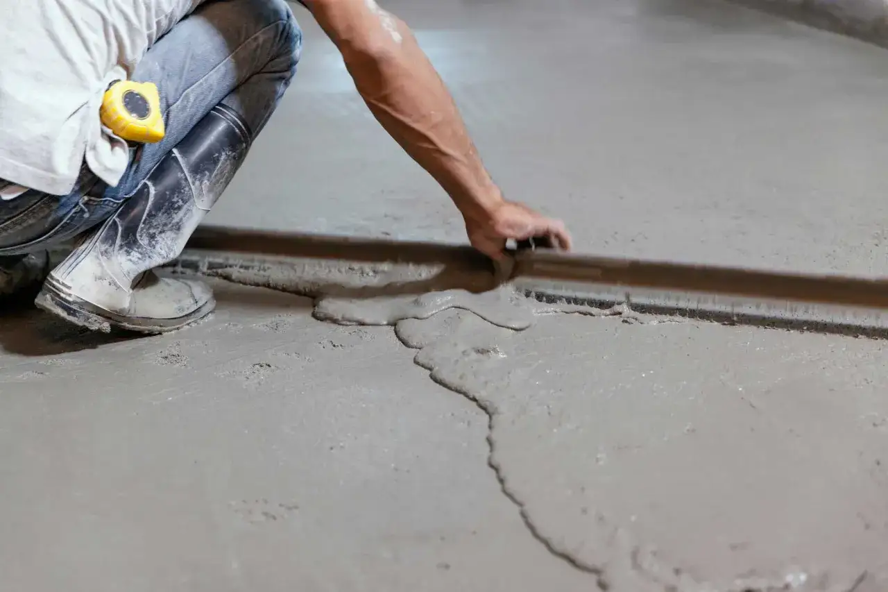 Obrero trabajando en como nivelar un suelo exterior, alisando cemento fresco con una regla.