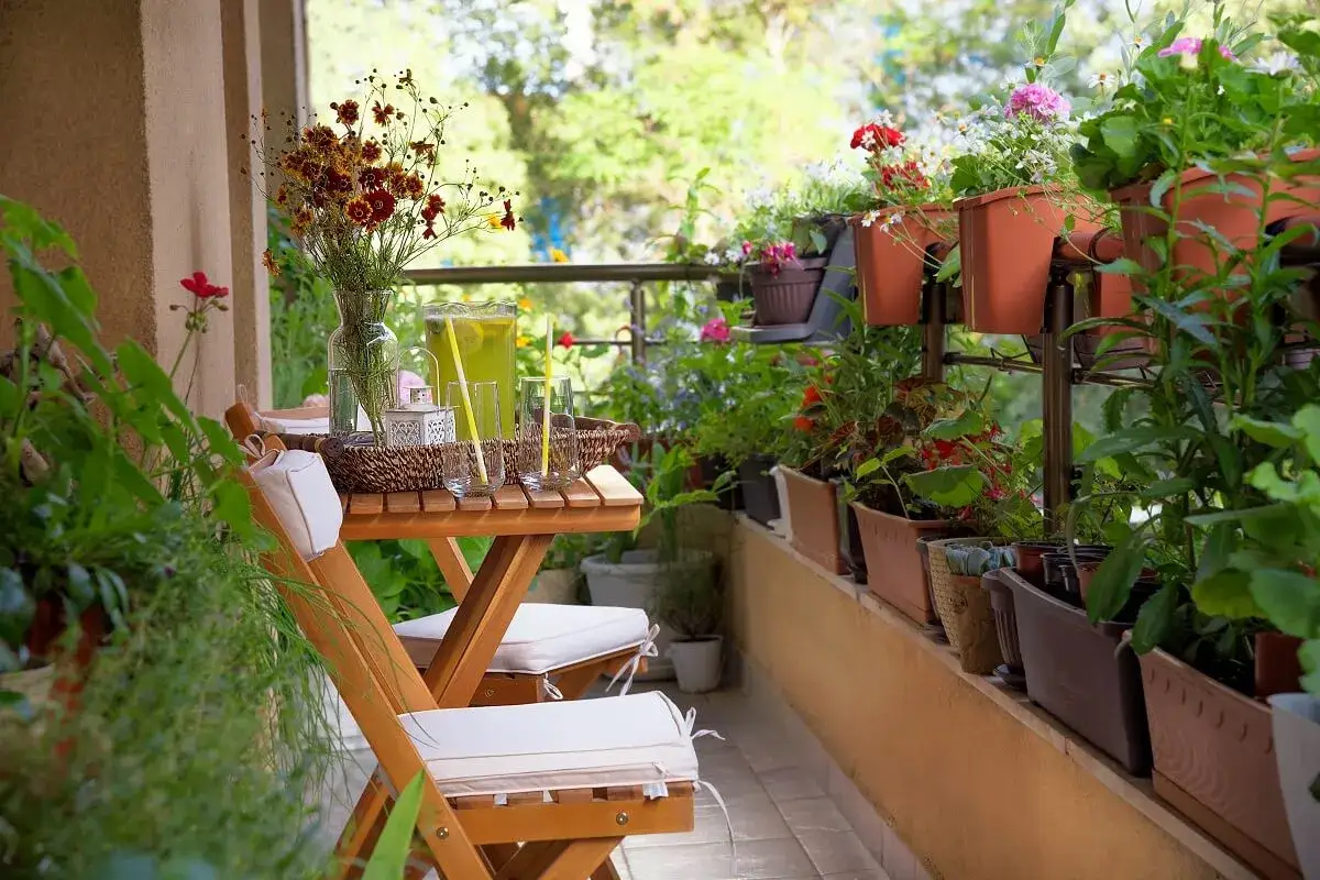 Un balc&oacute;n acogedor con mini balcones decoraci&oacute;n, mesa de madera, sillas y muchas plantas verdes y flores.