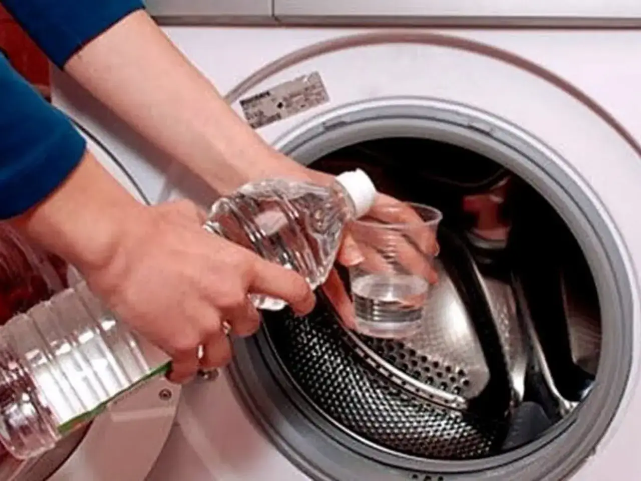 Manos vierten vinagre en lavadora para limpieza profunda. Un método natural para limpiar lavadora vinagre y bicarbonato.