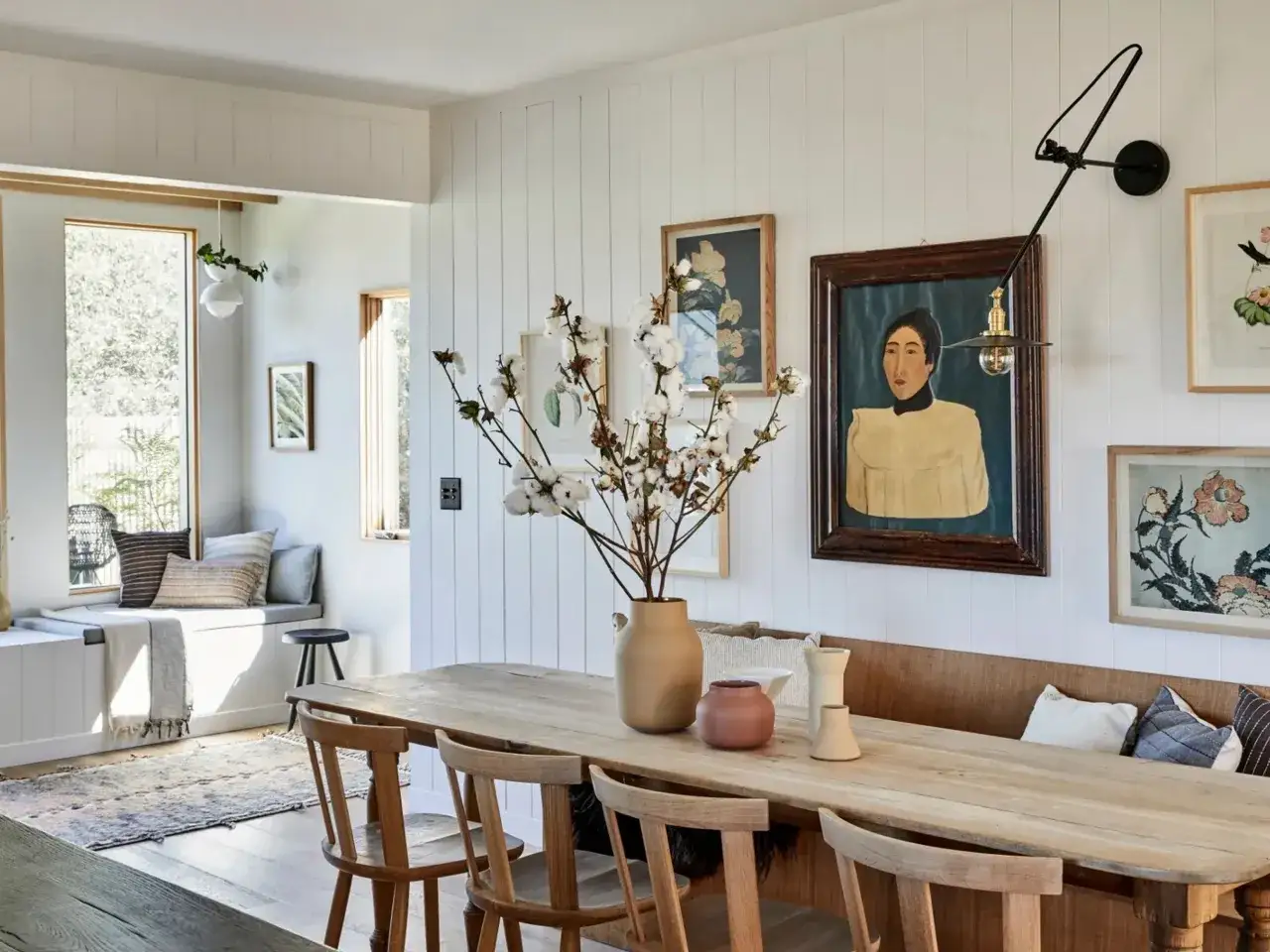 Amplio espacio alrededor de la mesa de comedor de madera, con sillas de madera, un banco tapizado y arte en las paredes.