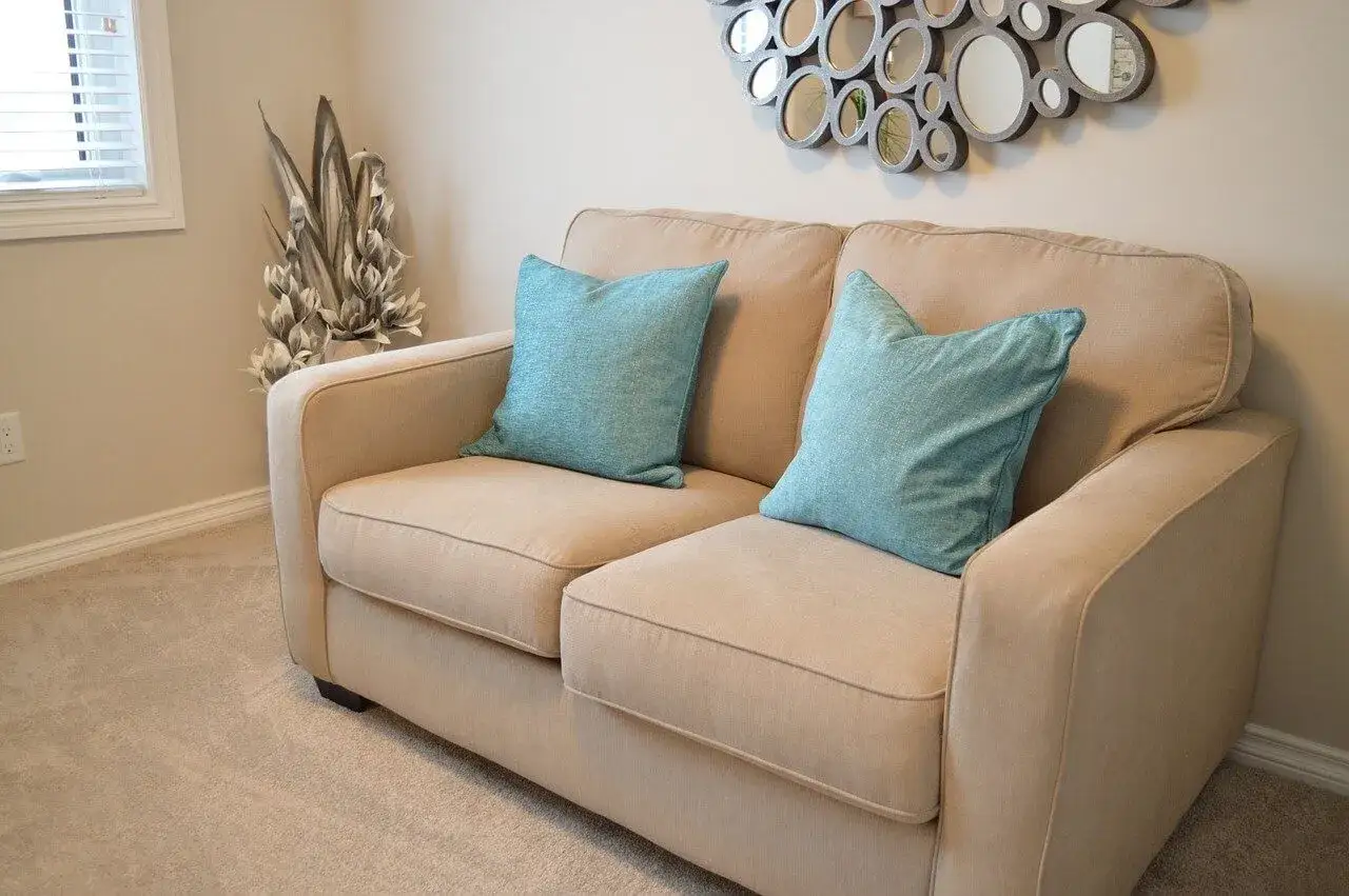 Sofá beige con cojines turquesas, ideal para aprender como tapizar un sofa y renovar tu hogar.